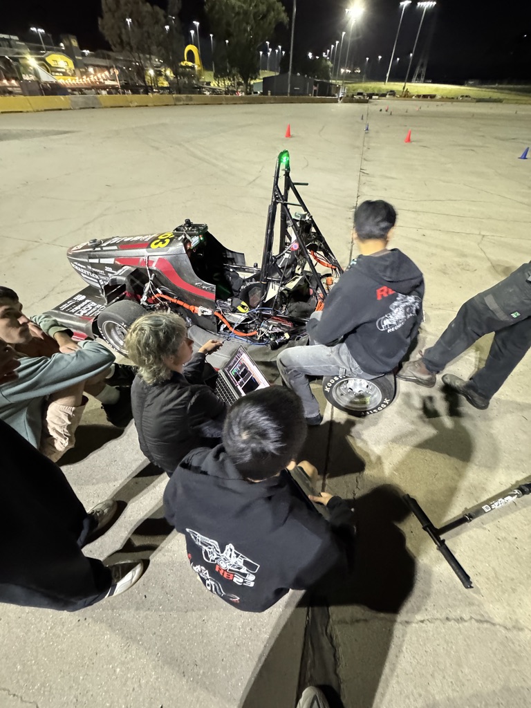 Redback Racing team members gathered around the parked race car at night